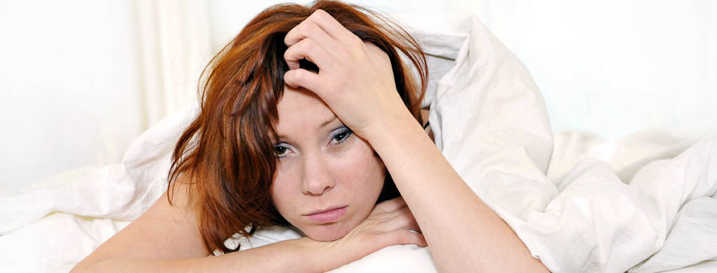 red hair woman on bed waking up with hangover and headache