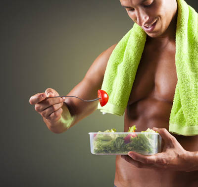 Smiling fitness man holding a bowl of fresh salad on black 