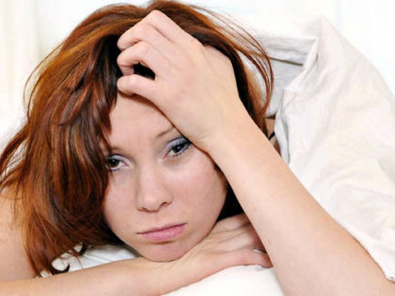 red hair woman on bed waking up with hangover and headache